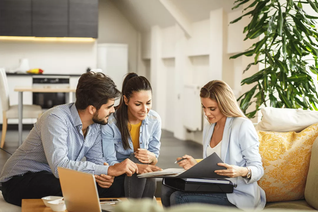 A couple sits inside a home with a business woman looking at a portfolio.